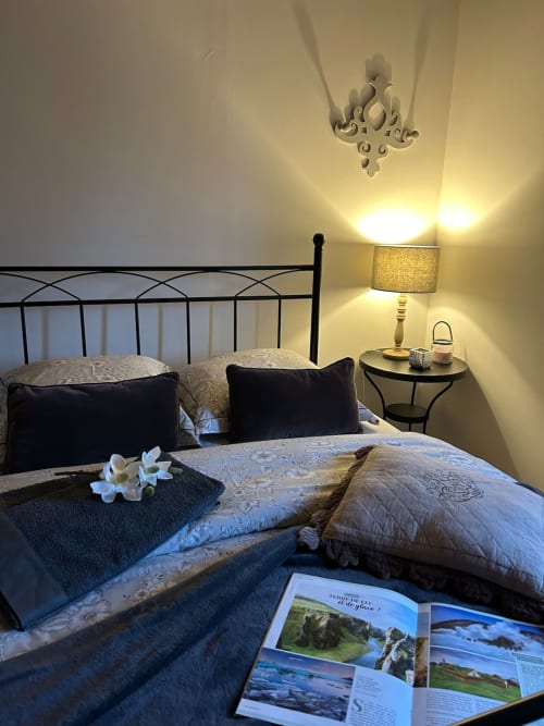 Chambre grise du gite Le Clos Mahiel avec lit en fer forgé, coussins, parure de draps élégant, lampe de chevet et magazines de voyage. Parures de draps comprises.