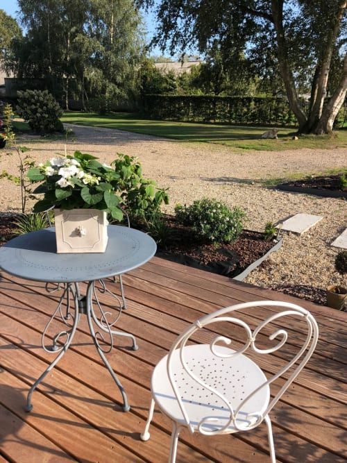 Vue sur le jardin de la terrasse du Clos Mahiel avec mobilier de bistrot blanc et jardinières fleuries