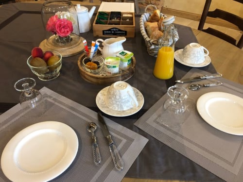 Table de petit-déjeuner élégante au Clos Mahiel avec assiettes blanches, fleurs fraîches, pâtisseries, jus de fruits et vue sur le jardin. Petits-déjeuners dans le jardin l'été. 