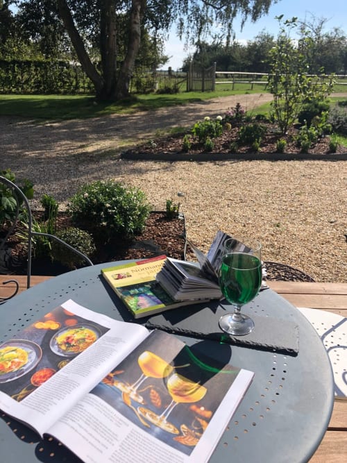 Table de salle à manger en plein air au Clos Mahiel avec livres de la région normande, Etretat, Honfleur, Deauville, Veules les roses, ...  magazines et verre rafraichissant dans le jardin