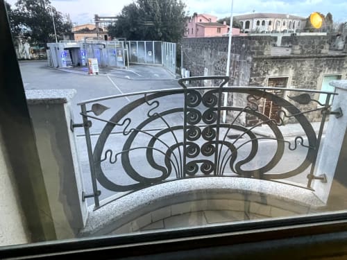 Ornate iron railing overlooking Orosei city street and historic buildings from apartment veranda