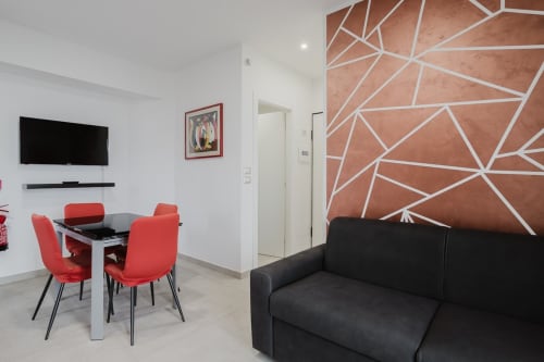 Modernes Wohnzimmer mit roten Esszimmerstühlen, schwarzem Sofa, geometrischer Wandkunst, Fernseher und Meerblick in Pietra Ligure