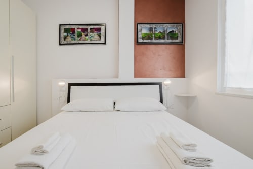 Modernes Schlafzimmer in der Residenza la Pietra in Pietra Ligure mit weißer Bettwäsche, schwarzem Kopfteil, gerahmten Kunstwerken und eleganter Atmosphäre