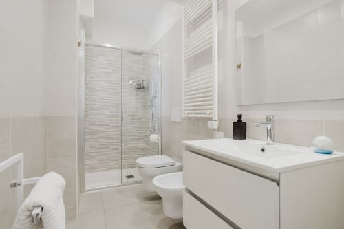 Modernes Badezimmer in der Residenza la Pietra in Pietra Ligure mit weißem Waschtisch, Glastür-Duschkabine und neutralen Fliesen