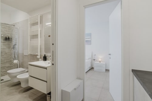 Modernes Badezimmer mit weißem Waschtisch, Toilette, beheiztem Handtuchhalter und Dusche in einer Wohnung in Pietra Ligure