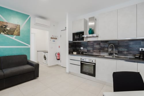 Moderne Küche und Wohnbereich im Apartment Residenza la Pietra mit weißen Schränken, schwarzer Rückwand und schwarzen Sofas