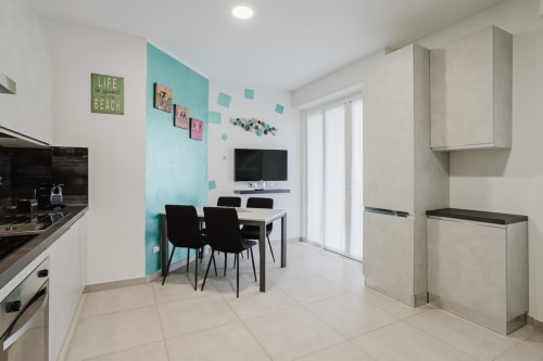 Moderner Wohn-Essbereich in der Residenza la Pietra mit türkiser Akzentwand, weißen Möbeln und schwarzem Esstisch