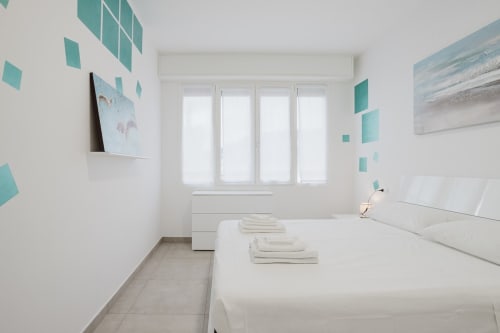 Helles modernes Schlafzimmer in der Residenza la Pietra in Pietra Ligure mit weißem Bett, türkisen Akzenten und Meerblick