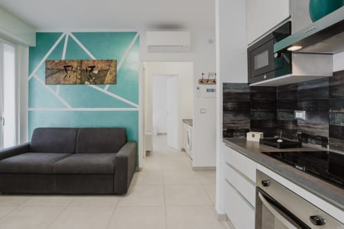 Moderne Küche und Wohnbereich in der Residenza la Pietra mit Türkis-Akzentwand, dunklem Sofa und zeitgenössischem schwarzen Design