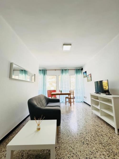 Sala de estar moderna en Rocamar, Santa Cruz de la Palma, con sofá oscuro, TV, zona de comedor y ventanas luminosas