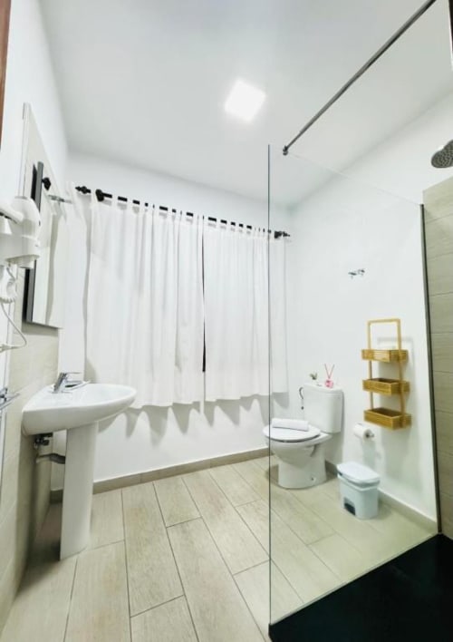 Baño moderno en Apartamentos Rocamar con ducha abierta, lavamanos pedestal y paredes blancas en Santa Cruz de la Palma