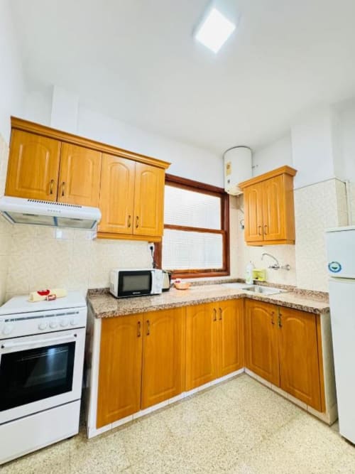 Cocina luminosa con muebles de madera dorada, encimera de granito y ventana en Apartamentos Rocamar, Santa Cruz de la Palma