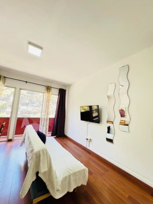 Dormitorio moderno en Apartamentos Rocamar con cama, TV, espejos ondulados, piso de madera y balcón con vistas a Santa Cruz de la