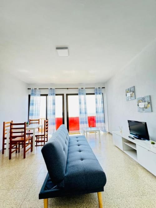 Moderno salón en Apartamentos Rocamar con sofá azul, televisor, zona de comedor y vistas al balcón en Santa Cruz de la Palma