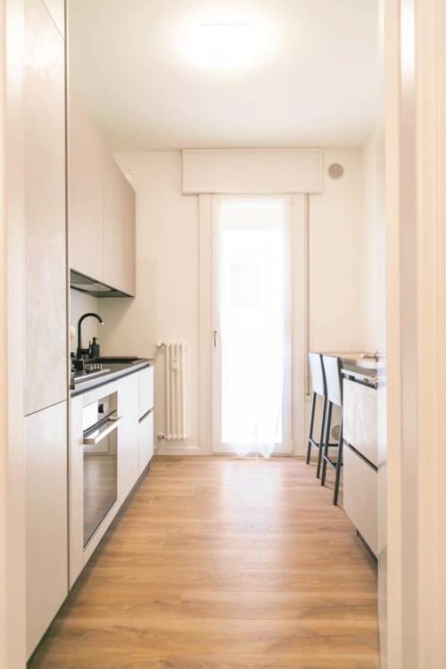 Modern galley kitchen in Ca' Martha apartment, Treviso, with white cabinetry, wooden floors, and bright natural light from