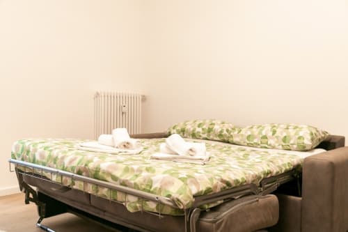 Opened sofa bed with green leaf patterned bedding and white towels rolled up in a Treviso apartment room