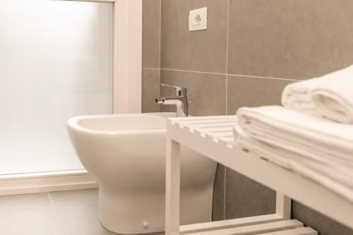 Moderno bagno con lavabo rotondo, rubinetto cromato, pareti piastrellate e asciugamani bianchi arrotolati presso Treviso Stays