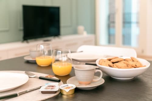 Tavola da colazione nell'appartamento di Treviso con succo d'arancia, biscotti, tazza di caffè e coperti, con vista sulla città sullo sfondo