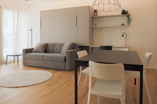 Interno moderno dell'appartamento Treviso Stays con divano grigio, tavolo da pranzo, pavimenti in legno e scaffali a parete in Ca' Borsa