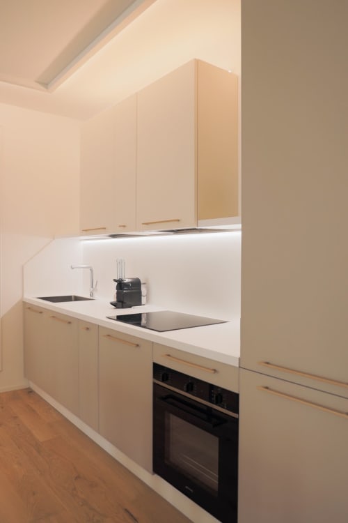 Cucina moderna nell'appartamento Ca' Borsa a Treviso: mobili in legno chiaro, piano di lavoro bianco, forno nero e piano cottura a induzione