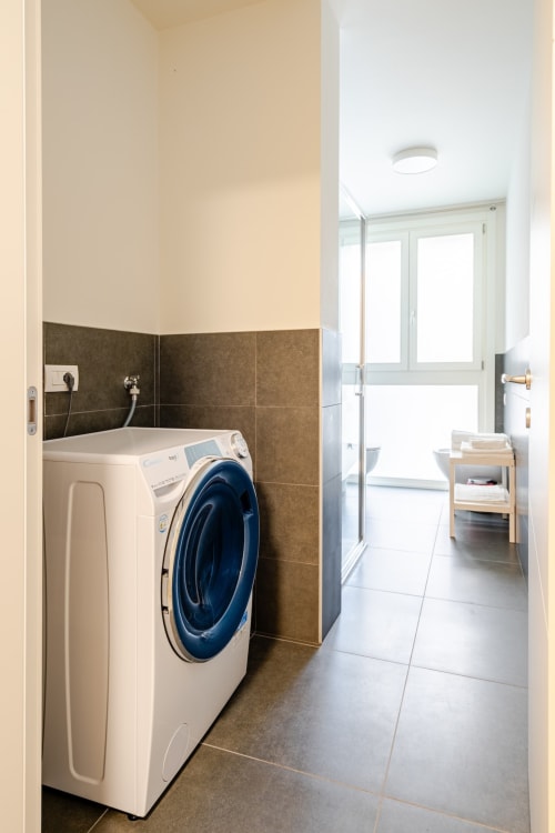 Modern laundry room in Ca' Borsa II apartment, Treviso with white front-load washing machine and brown tile backsplash