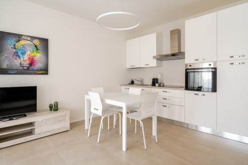 Modern open-plan kitchen and dining area in Ca' Borsa II apartment, Treviso with white cabinetry, induction cooktop, and
