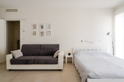 Modern studio apartment in Treviso with dark sofa, white bed, and botanical wall decor