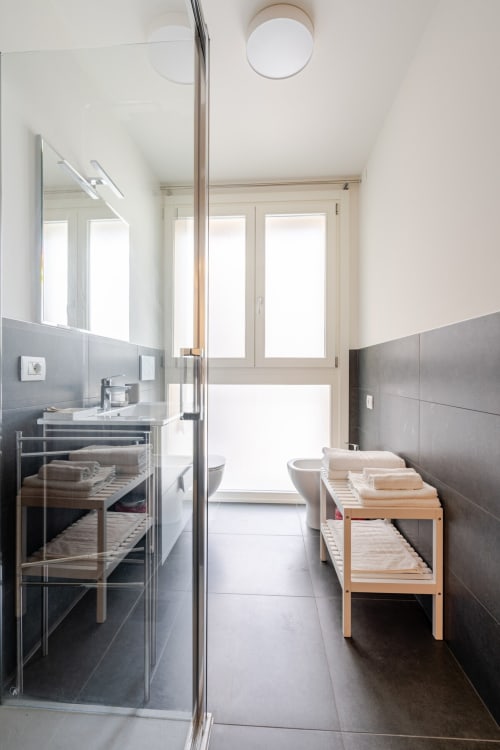Modern bathroom at Ca' Borsa II in Treviso with walk-in shower, sink, toilet, and wooden storage shelves with towels