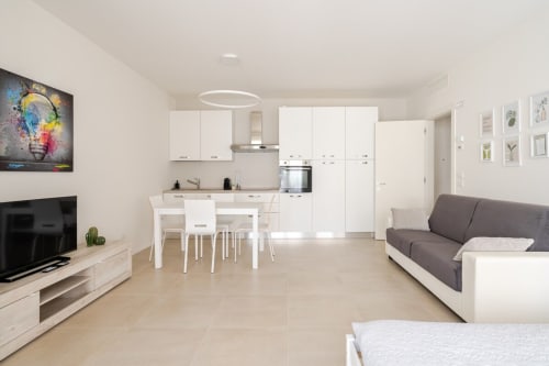 Modern open-plan apartment in Treviso with white kitchen, dining area, sofa, and TV in historic city center