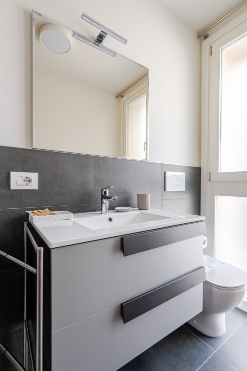Modern bathroom in Ca' Borsa II apartment, Treviso featuring white vanity, dark tile, mirror and toilet