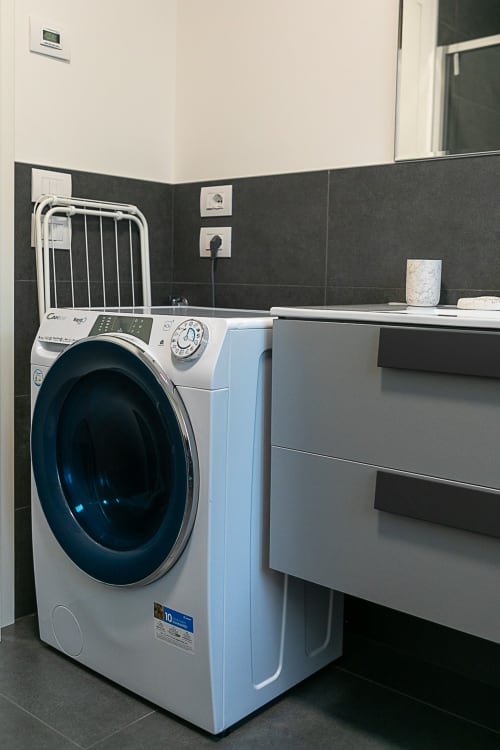Moderna lavatrice nel bagno dell'appartamento Ca Borsa III a Treviso, con pareti in piastrelle scure e mobile lavabo grigio.