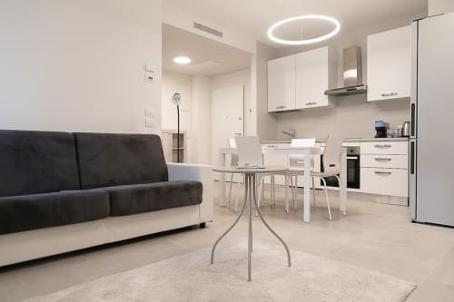 Modern apartment living space in Treviso with black sofa, white dining table, fully equipped kitchen, and circular ceiling
