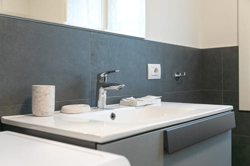 Lavabo moderno con rubinetto cromato, saponiera in marmo e pareti rivestite in scuri piastrelloni nell'appartamento Ca Borsa III, Treviso