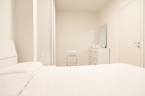 Camera da letto minimalista presso Treviso Stays con biancheria bianca, cassettiera, specchio e sedia