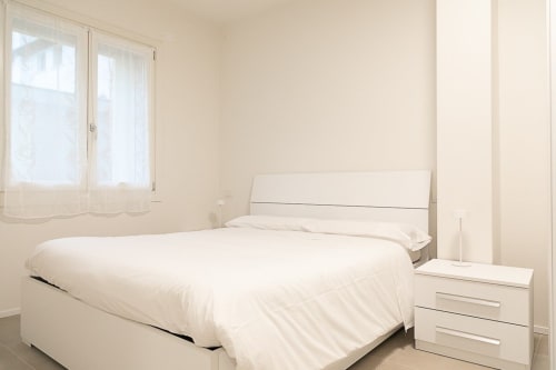 Camera luminosa e minimalista in Ca Borsa III a Treviso con letto bianco, comodino e vista sulla città