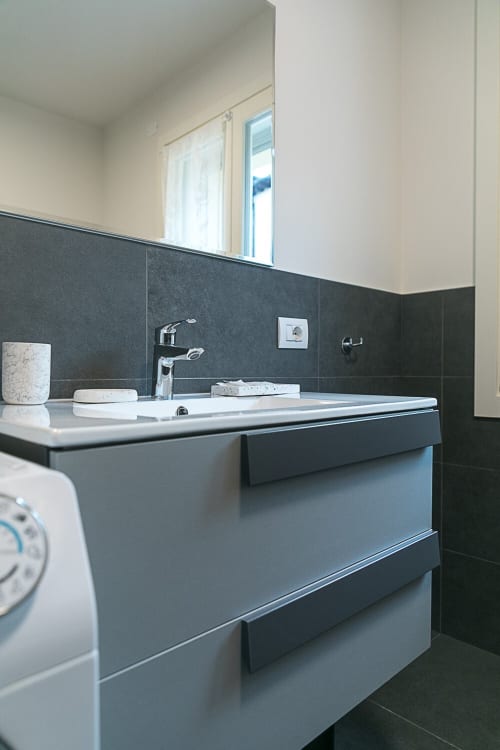 Bagno moderno nell'appartamento Ca Borsa III di Treviso con piastrelle grigie, lavabo bianco e rubinetteria cromata.