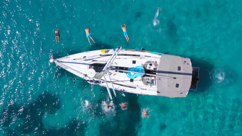 Aerial view of white sailboat with guests swimming in turquoise waters near Fasano, Italy