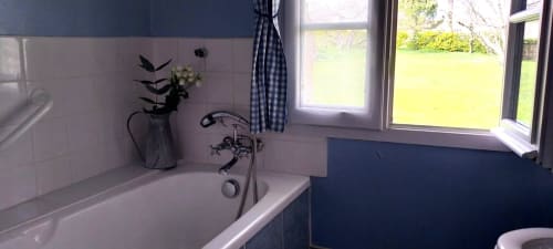 Bright bathroom with white tiles, freestanding bathtub, vintage faucet, potted plant, and garden views through windows at La