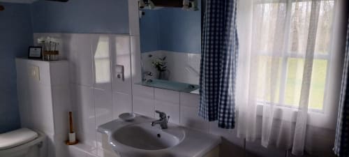 Clean bathroom with white sink, mirror, and blue accents at Le Séchoir cottage in Monmarvès