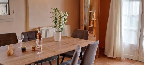 Dining room in Le Séchoir cottage at La Barrat with wooden table, brown chairs, white flowers, and garden view doors