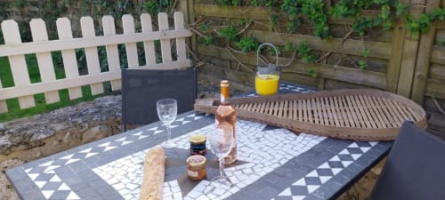 Outdoor patio at Le Séchoir cottage with garden view, featuring dining table, beverages, bread, and wooden lounger at La