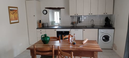 Bright kitchen-dining area in La Crèche cottage at La Barrat, Monmarvès, with wooden table, white cabinetry, and modern
