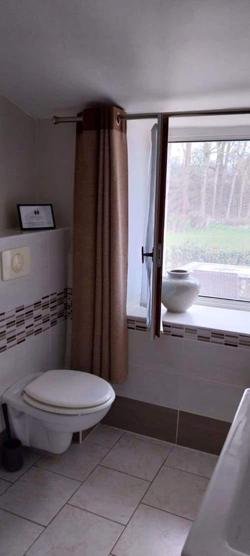 Modern bathroom in La Crèche cottage at La Barrat B&B, Monmarvès, with toilet, brown curtain, window overlooking grounds, and