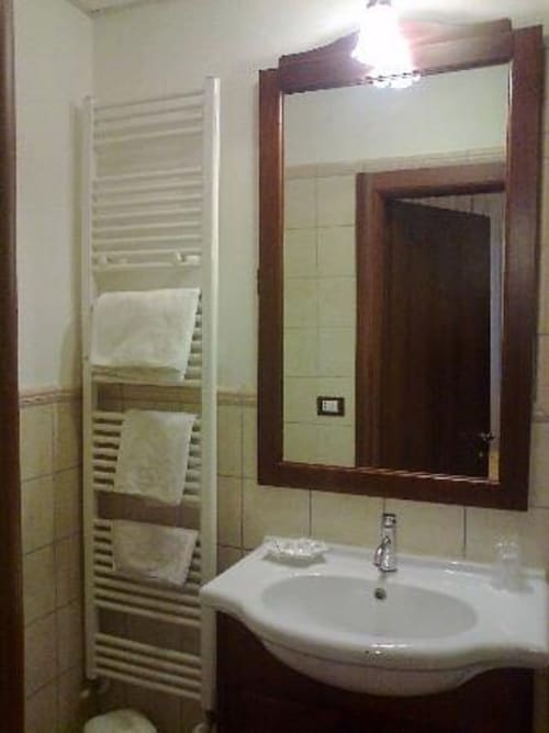 Modern bathroom with white pedestal sink, framed mirror, heated towel rack, and cream tile walls at Il Casale di Nanni B&B in