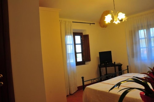 Bright yellow bedroom at Il Casale di Nanni in Lucca with double bed, TV, desk, and garden views through windows