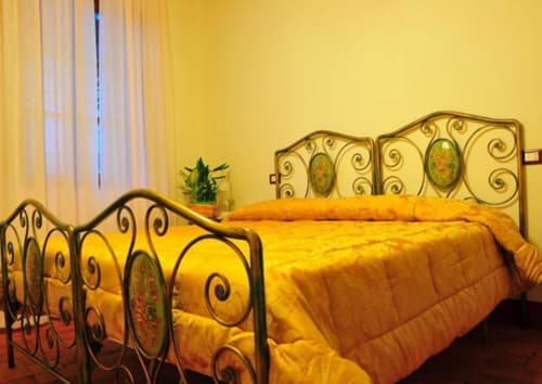 Bright yellow bedroom with ornate iron bed frame at Il Casale di Nanni B&B in Lucca, Italy, featuring garden view and modern