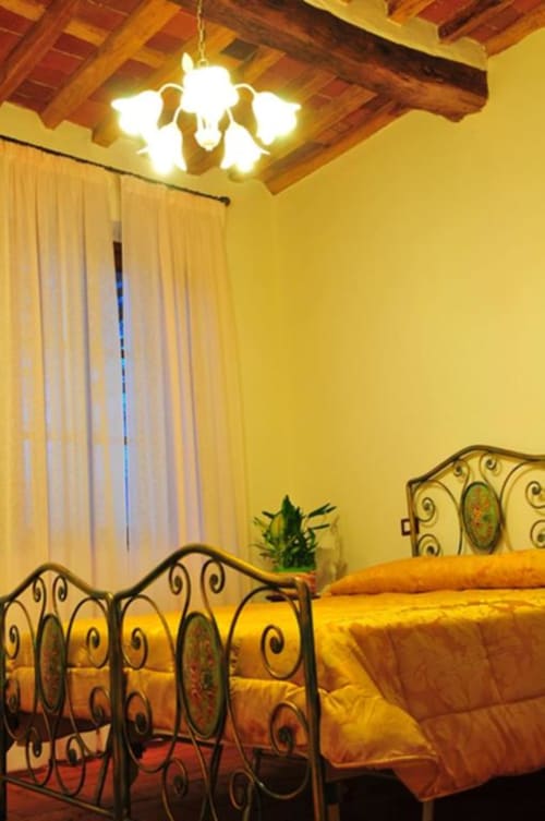 Warm, inviting double bedroom at Il Casale di Nanni B&B in Lucca with ornate iron bed frame and yellow bedding under wooden