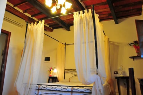 Luxurious four-poster canopy bed with white curtains in Suite at Il Casale di Nanni, Lucca - exposed wooden ceiling beams,