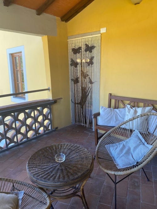 Bright yellow suite balcony at Il Casale di Nanni in Lucca with wicker chairs, round table, and beaded curtain doorway