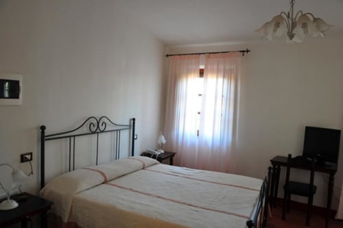 Triple room at Il Casale di Nanni B&B in Lucca with metal bed, TV, desk, and mountain views through sheer curtains